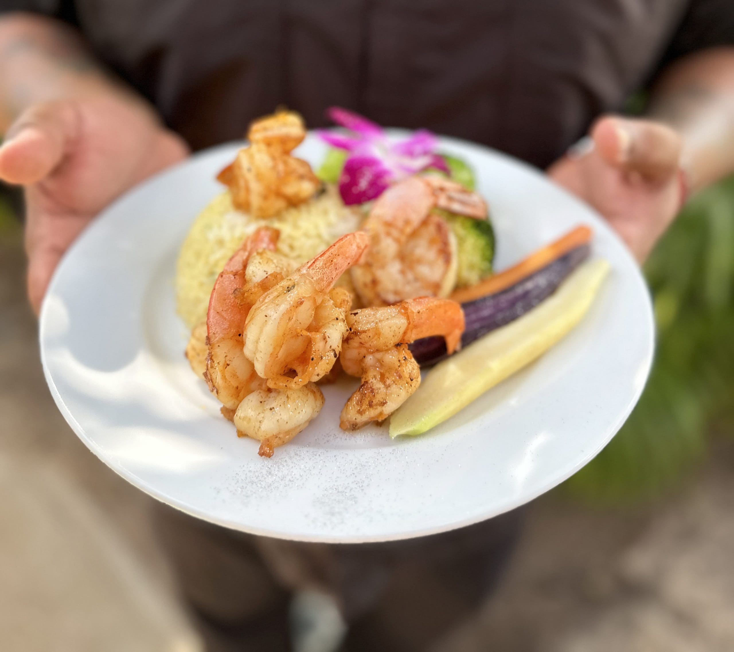 Seasoned Caribbean shrimp plated over golden rice with grilled vegetables and orchid garnish, served at Carambola at the Blue in Vieques, Puerto Rico